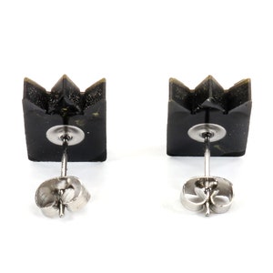 May include: A pair of black crown-shaped stud earrings. Each earring features a square base with a three-point crown design. The earrings have silver-colored posts and butterfly backs, set against a white background.