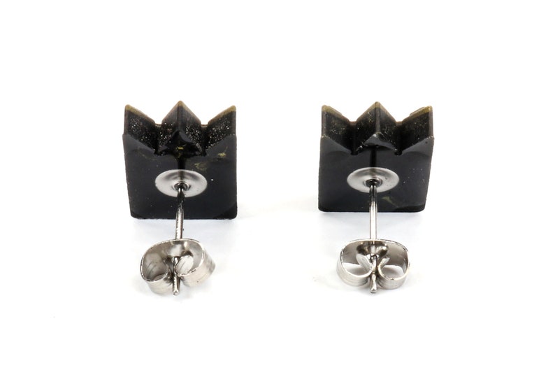 May include: A pair of black crown-shaped stud earrings. Each earring features a square base with a three-point crown design. The earrings have silver-colored posts and butterfly backs, set against a white background.