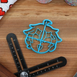May include: A blue plastic cookie cutter shaped like a cartoon character with green hair and a shovel. The character has a surprised expression.