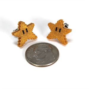 May include: A pair of gold star-shaped earrings with black eyes. The earrings are about the size of a US dime.