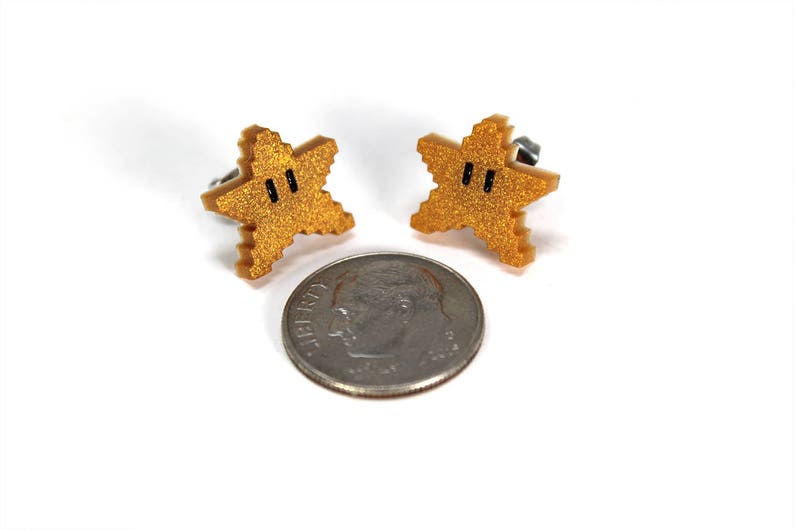 May include: A pair of gold star-shaped earrings with black eyes. The earrings are about the size of a US dime.