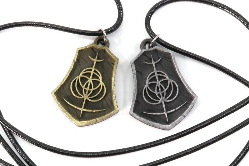 May include: Two necklaces with matching pendants. The pendants are shield-shaped with a black and silver design. One pendant is gold and the other is silver.