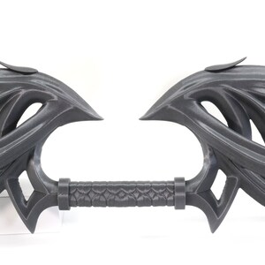 May include: A 3D printed, gray, decorative sword with a detailed, intricate design. The sword has a long, thin handle and two large, curved blades.
