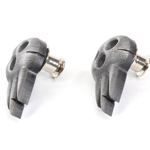Op de afbeelding: Twee zilveren schedelvormige gitaarbandknopen met een geborstelde metalen afwerking.