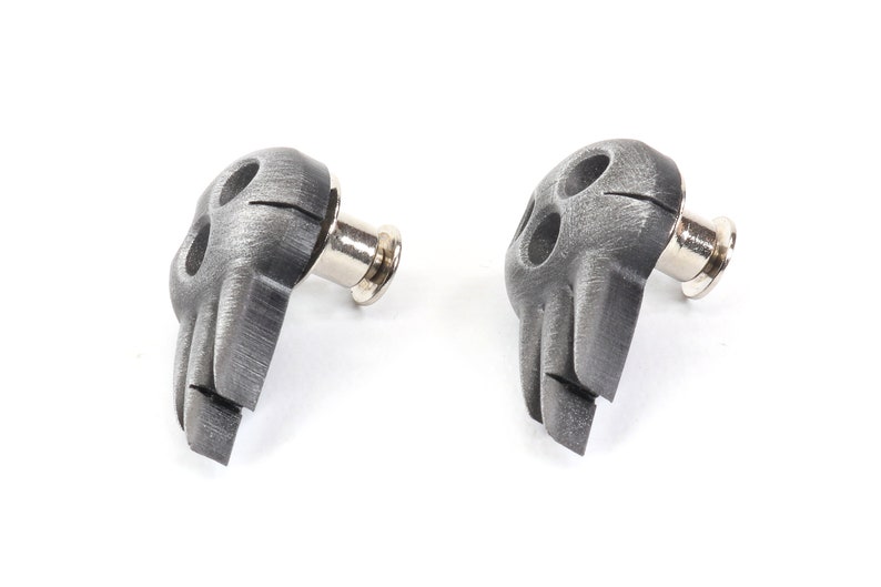 Op de afbeelding: Twee zilveren schedelvormige gitaarbandknopen met een geborstelde metalen afwerking.