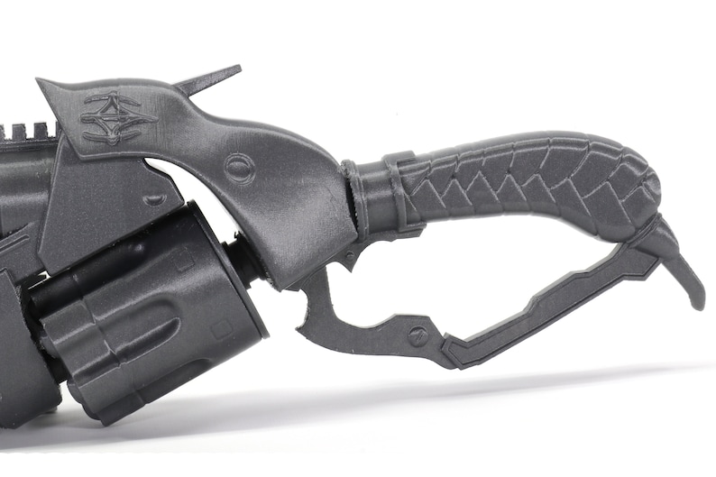 May include: A gray 3D printed model of a futuristic weapon with a textured handle and a trigger.