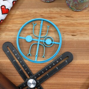 May include: A blue plastic cookie cutter shaped like a circle with a design inside. The design includes two circles, two curved lines, and two small loops.