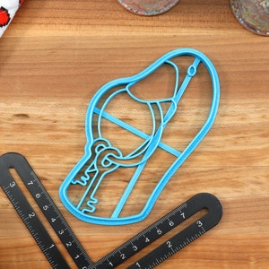 May include: A blue plastic cookie cutter shaped like a slipper with a keyhole and key design.