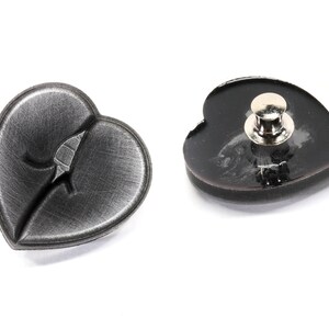 May include: Two black heart-shaped pins. One pin has a brushed metal finish and the other has a glossy finish. Both pins have a silver metal clasp on the back.
