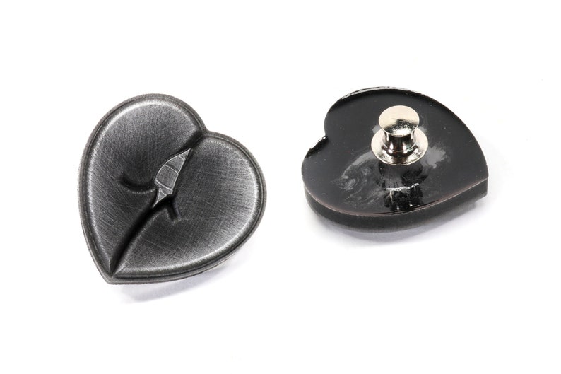 May include: Two black heart-shaped pins. One pin has a brushed metal finish and the other has a glossy finish. Both pins have a silver metal clasp on the back.
