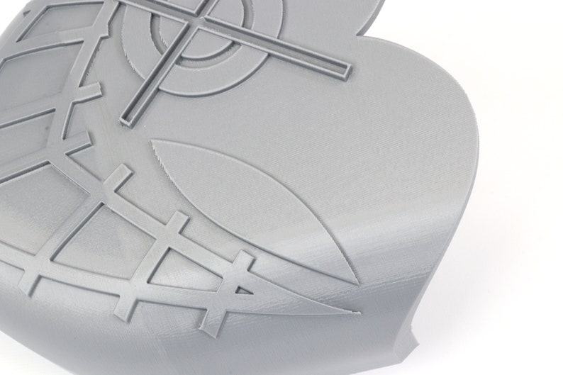 May include: A close-up of a gray, 3D-printed object with a complex geometric design. The design includes crosshairs, a grid pattern, and stylized leaf shapes. The object has a smooth, matte finish and is set against a white background.
