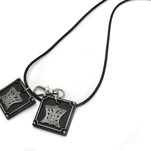 Puede incluir: Un collar de cord&oacute;n negro con un colgante de metal plateado que presenta un dise&ntilde;o detallado. El colgante est&aacute; unido a un cierre de metal plateado.