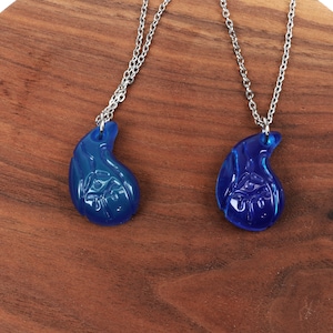May include: Two matching blue glass necklaces with silver chains. Each pendant is shaped like a teardrop with a detailed design.