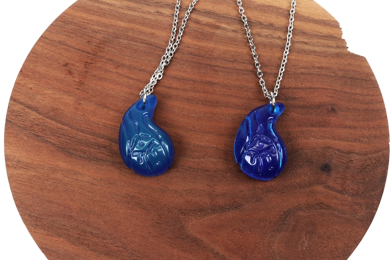 May include: Two matching blue glass necklaces with silver chains. Each pendant is shaped like a teardrop with a detailed design.