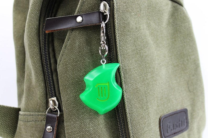 May include: A green plastic keychain charm shaped like a leaf with a harp symbol inside. The charm is attached to a silver chain and is hanging from a green canvas bag.