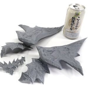 May include: Five grey 3D printed pieces of a dragon wing, with a can of Japanese beer in the background.