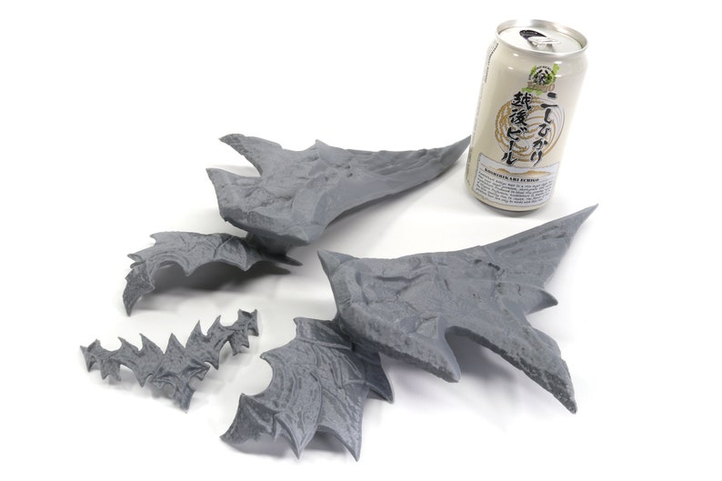 May include: Five grey 3D printed pieces of a dragon wing, with a can of Japanese beer in the background.