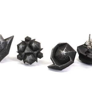 May include: Four silver-colored earrings with geometric designs. The earrings are in the shape of a triangle, a star, a circle, and a crescent moon.