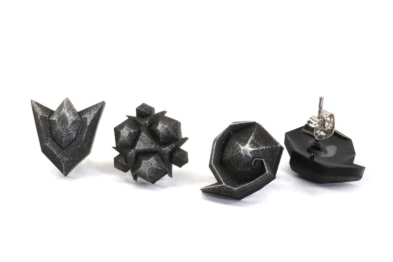 May include: Four silver-colored earrings with geometric designs. The earrings are in the shape of a triangle, a star, a circle, and a crescent moon.