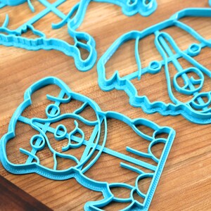 May include: A set of four blue plastic cookie cutters shaped like dogs. The cutters are on a wooden surface.
