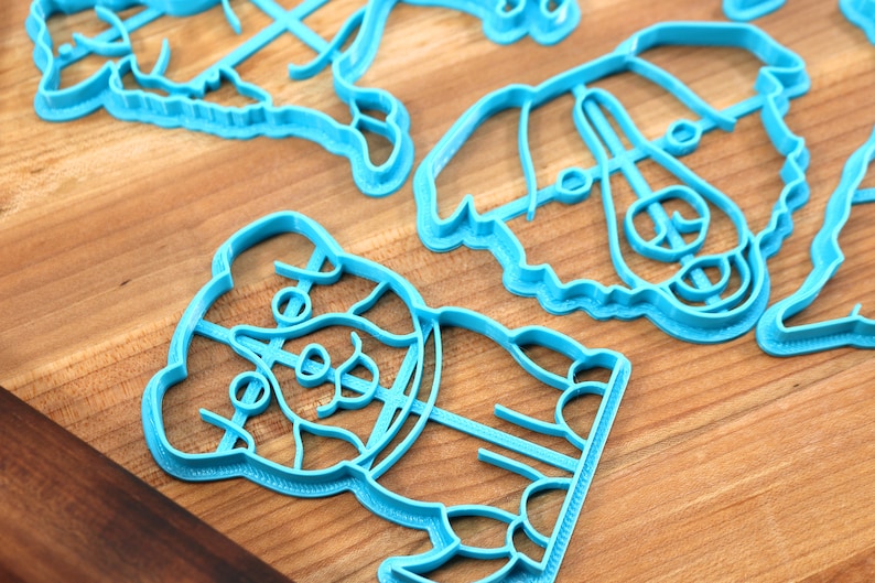 May include: A set of four blue plastic cookie cutters shaped like dogs. The cutters are on a wooden surface.