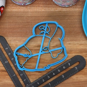 May include: A blue plastic cookie cutter shaped like a cartoon character wearing a hat with a hammer and sickle symbol.