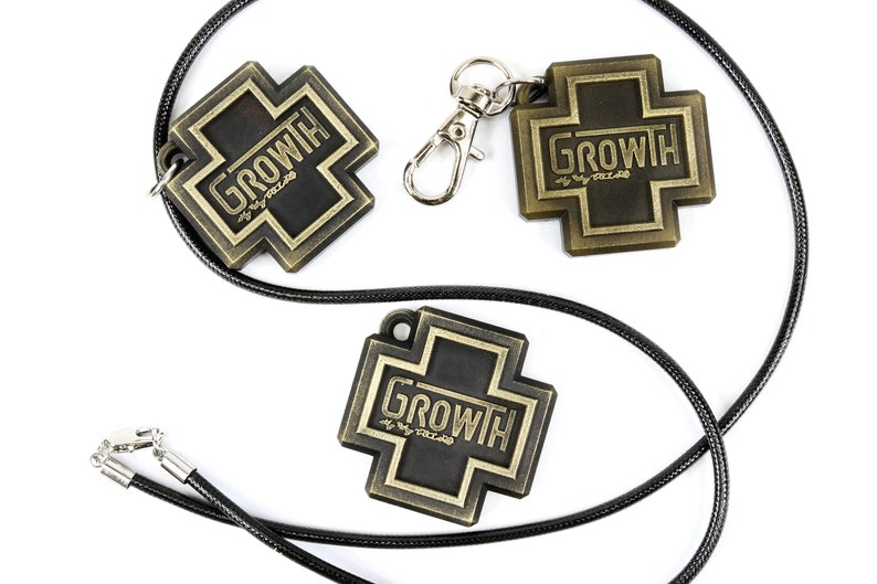 May include: Two gold-colored metal cross charms with the word "GROWTH" on them. One charm is on a black cord necklace and the other is on a silver key chain.