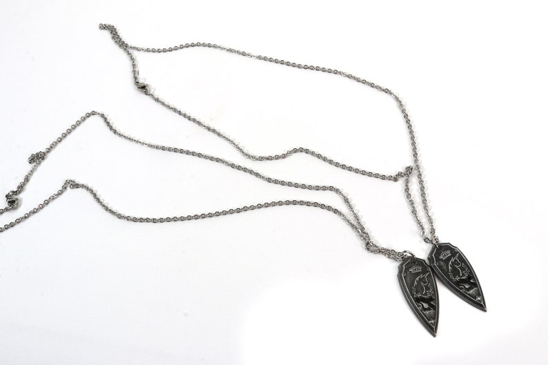 May include: Two silver chains with matching pendants. Each pendant is a silver teardrop shape with a detailed design of a mythical creature.