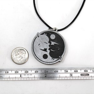 May include: A silver yin yang pendant necklace with a black cord. The pendant features a stylized yin yang symbol with a black and white design. The pendant is about 2 inches in diameter.