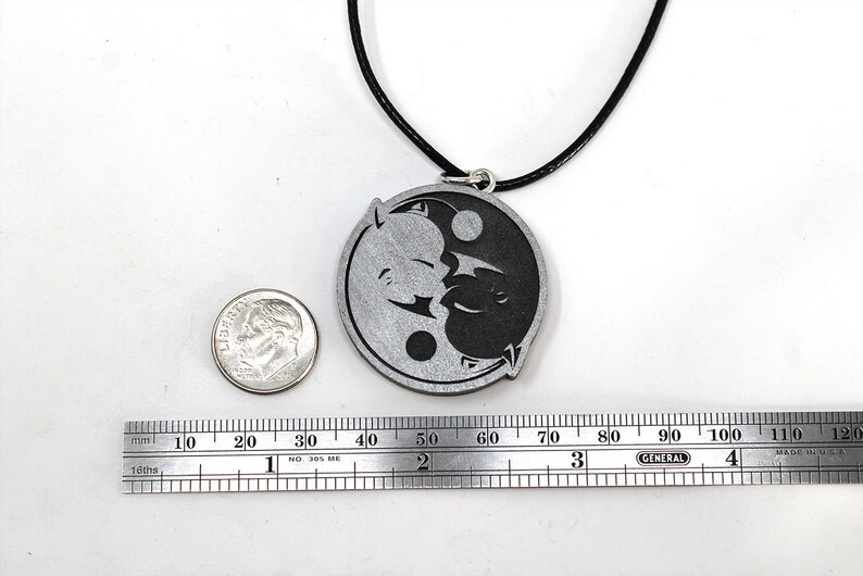 May include: A silver yin yang pendant necklace with a black cord. The pendant features a stylized yin yang symbol with a black and white design. The pendant is about 2 inches in diameter.