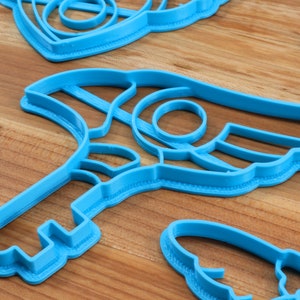 May include: A set of blue plastic cookie cutters in various shapes, including a crescent moon, a star, and a key. The cutters are on a wooden surface.