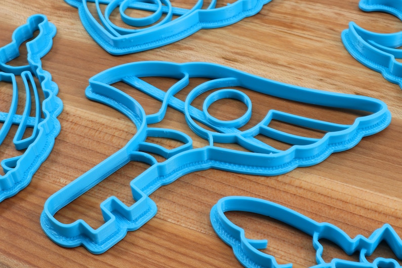 May include: A set of blue plastic cookie cutters in various shapes, including a crescent moon, a star, and a key. The cutters are on a wooden surface.