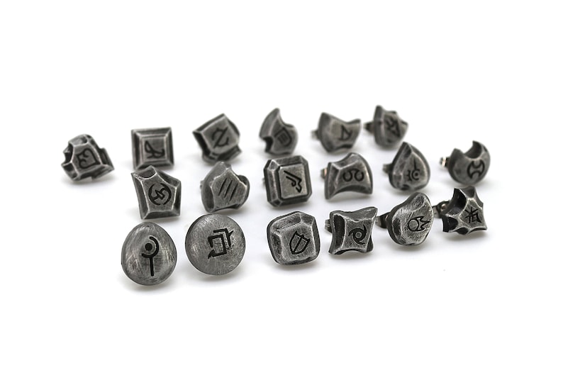 Puede incluir: Un conjunto de 17 dijes de metal plateado con varios s&iacute;mbolos y dise&ntilde;os. Los dijes son peque&ntilde;os y tienen un acabado texturizado.