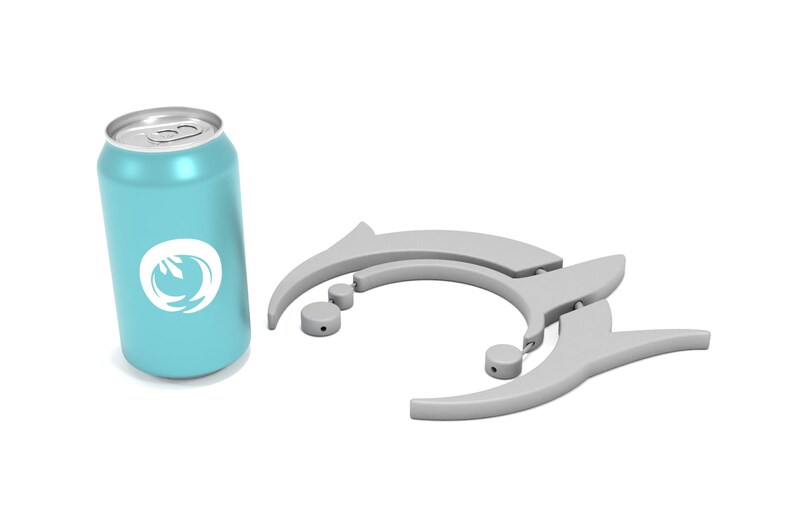 May include: A light blue beverage can with a white logo and a silver top. Next to it are two gray drink holders with a dolphin-like design, along with two small gray circular pieces. The items are on a white background.