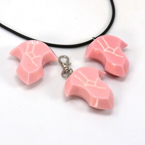 May include: Three pink resin pendants with a white Gemini zodiac symbol. The pendants are attached to a black cord necklace and a silver key chain.