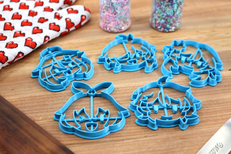 May include: Five blue plastic cookie cutters shaped like cartoon characters. The cutters are on a wooden surface.
