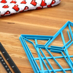 Puede incluir: Un cortador de galletas de pl&aacute;stico azul en forma de estrella con un dise&ntilde;o geom&eacute;trico. El cortador est&aacute; sobre una superficie de madera.