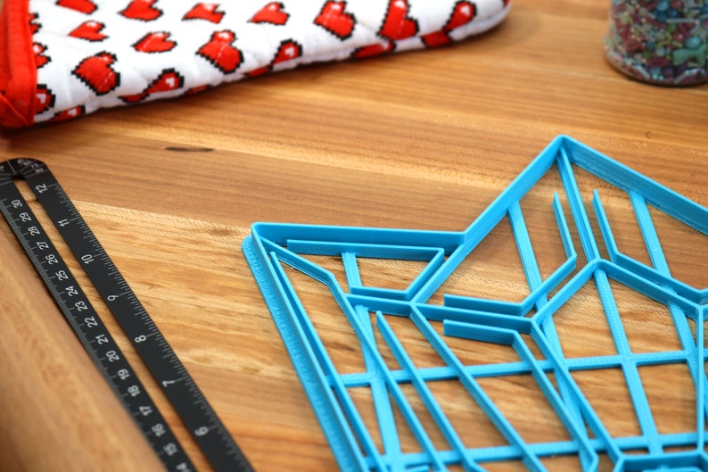 Puede incluir: Un cortador de galletas de pl&aacute;stico azul en forma de estrella con un dise&ntilde;o geom&eacute;trico. El cortador est&aacute; sobre una superficie de madera.