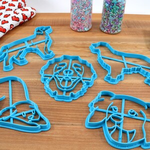 May include: A set of five blue plastic dog-shaped cookie cutters. The cutters are in the shape of a dog's head, a dog's body, and a dog's paw.