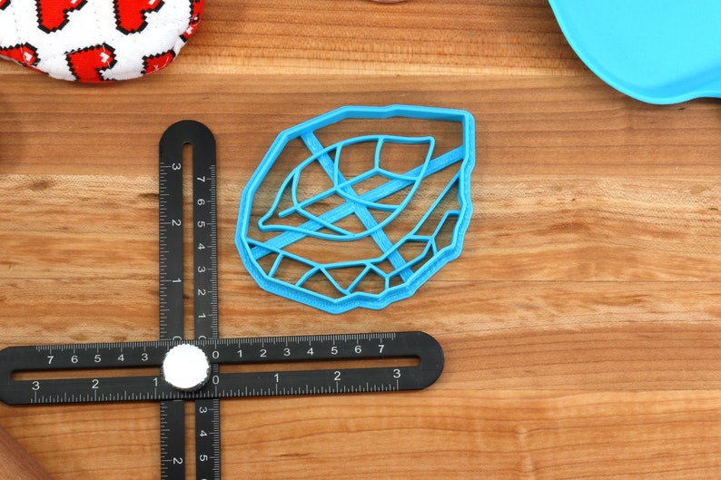 May include: A blue plastic leaf-shaped cookie cutter. The cutter has a detailed design with a raised edge.