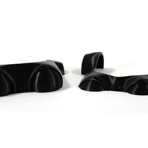 May include: Two black plastic pieces with rounded edges and a raised center section. The pieces are designed to be joined together to form a larger piece.