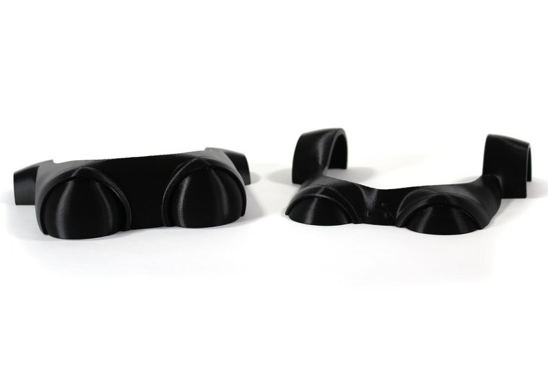 May include: Two black plastic pieces with rounded edges and a raised center section. The pieces are designed to be joined together to form a larger piece.