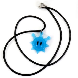 May include: A blue star-shaped pendant with a smiling face hangs from a black cord necklace.