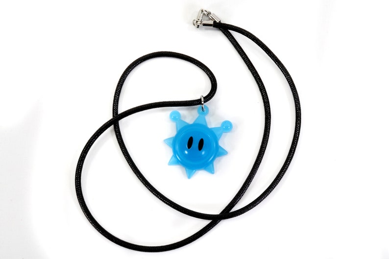 May include: A blue star-shaped pendant with a smiling face hangs from a black cord necklace.
