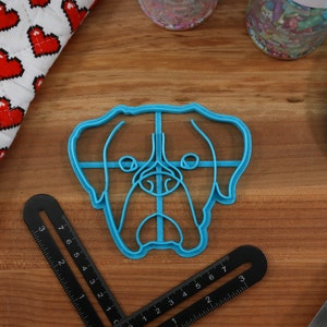 May include: A blue plastic cookie cutter shaped like a dog's head. The cutter has a detailed outline of the dog's face, including the eyes, nose, and mouth.