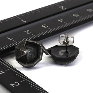 May include: A pair of silver geometric stud earrings with a black finish. The earrings are shown on a black ruler.