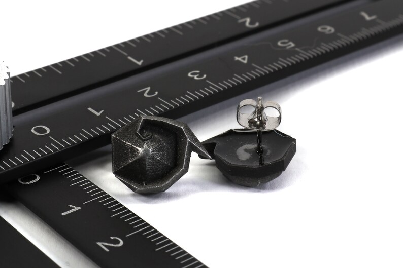 May include: A pair of silver geometric stud earrings with a black finish. The earrings are shown on a black ruler.