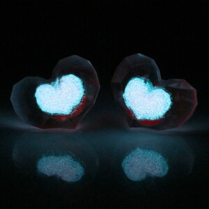 Puede incluir: Dos adornos de vidrio transparente en forma de coraz&oacute;n con un coraz&oacute;n de purpurina azul brillante dentro de cada uno. Los adornos est&aacute;n sobre una superficie negra.