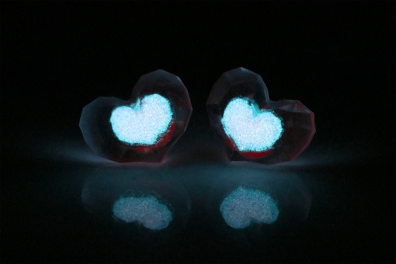 Puede incluir: Dos adornos de vidrio transparente en forma de coraz&oacute;n con un coraz&oacute;n de purpurina azul brillante dentro de cada uno. Los adornos est&aacute;n sobre una superficie negra.
