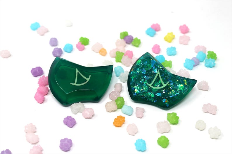 Puede incluir: Dos dados de resina verde con un dise&ntilde;o de velero. Un dado es verde s&oacute;lido, y el otro tiene purpurina iridiscente incrustada en la resina.
